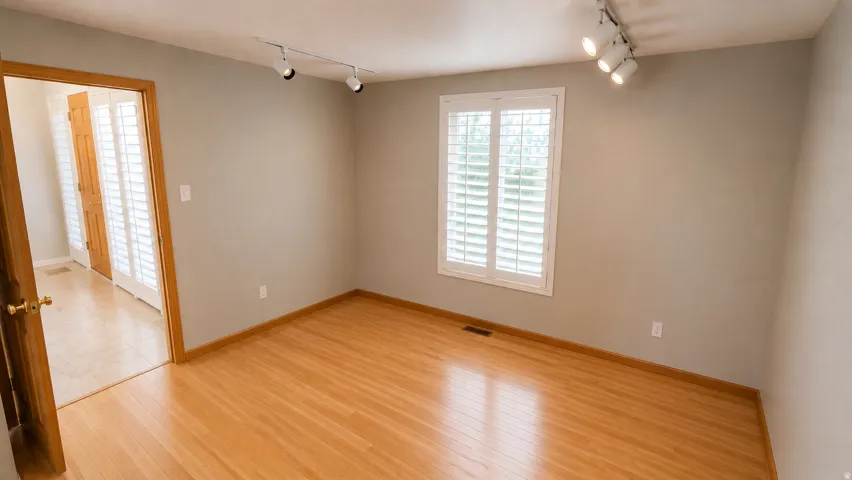 Hardwood flooring, natural wood door frames, white plantation shutters, and track lighting