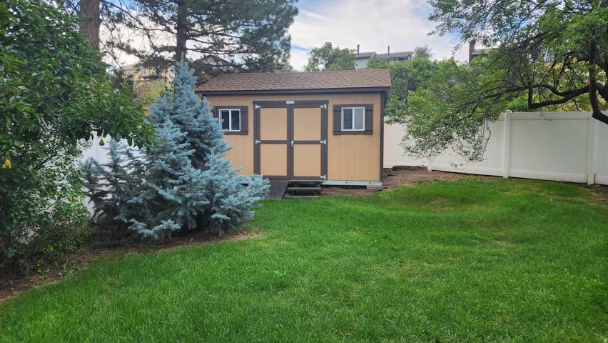 Expansive lawn featuring a storage shed with dual doors, white vinyl fencing, and mature landscaping