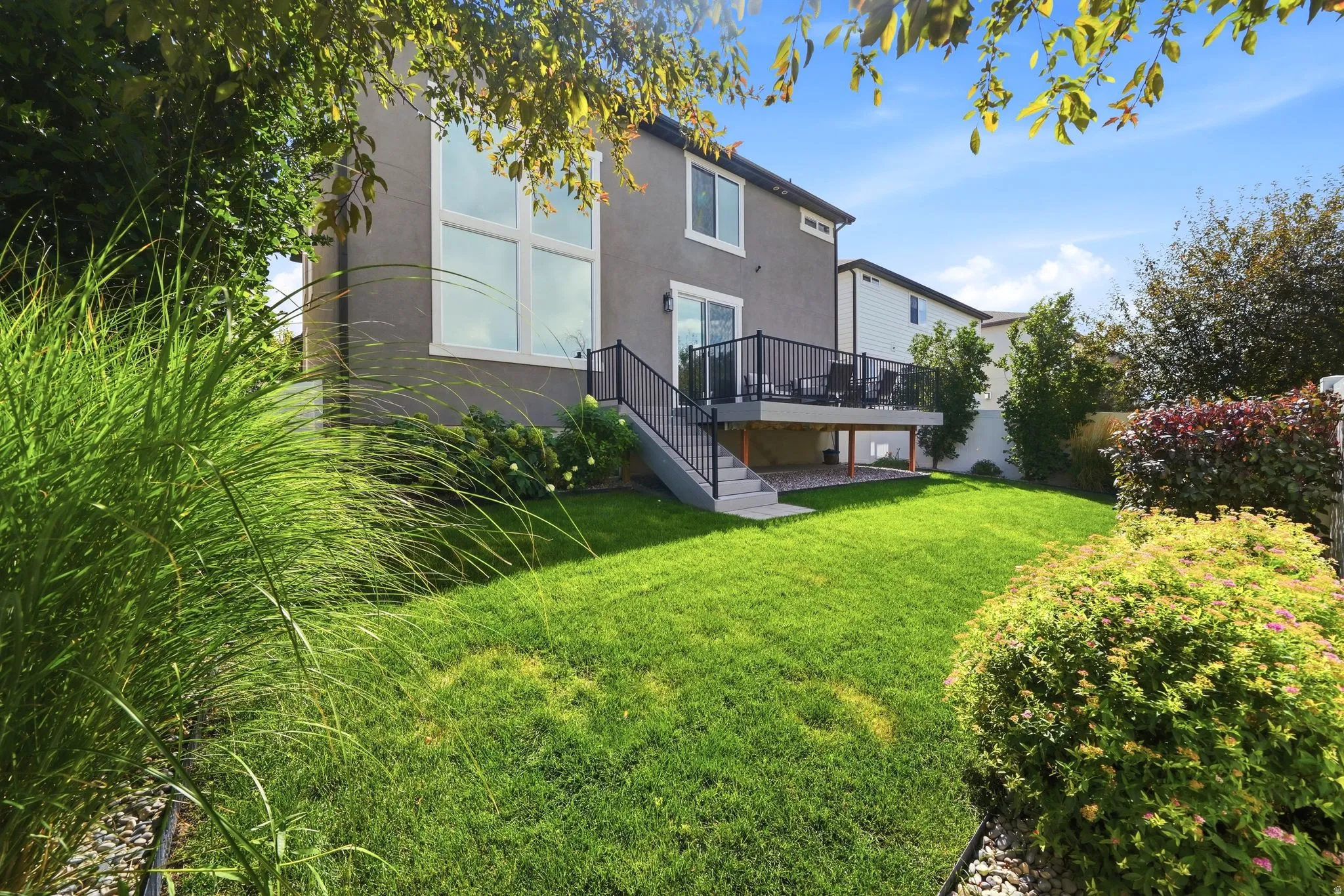 Expansive backyard featuring a manicured lawn, a raised deck with metal railings, a sliding glass door, and a stucco exterior