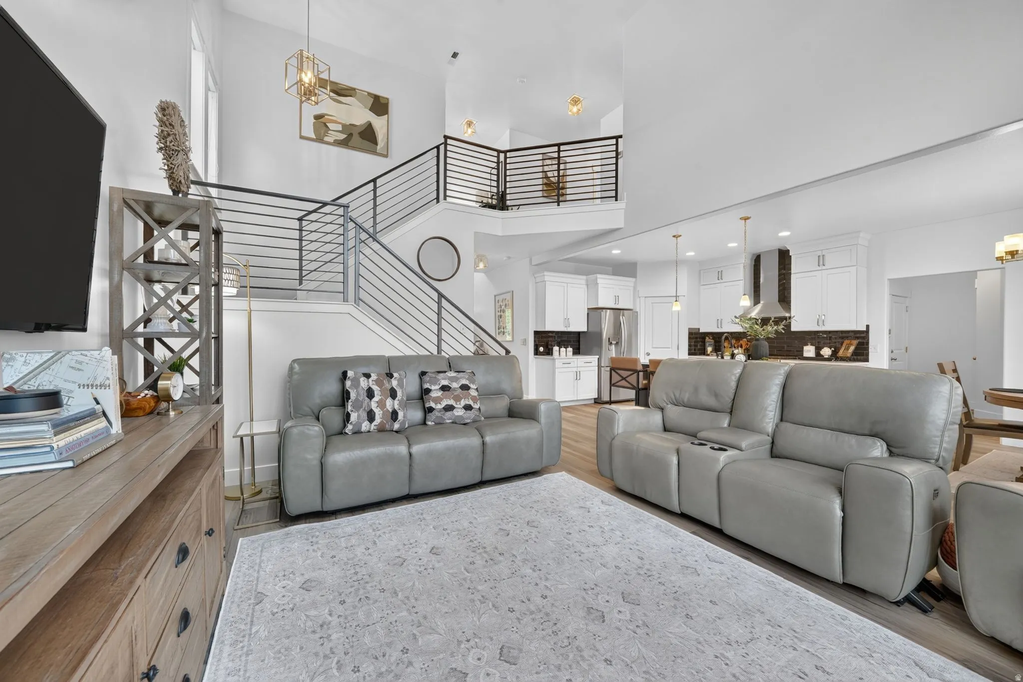 Open-concept living area featuring a two-story ceiling, modern staircase with horizontal railings, and recessed lighting