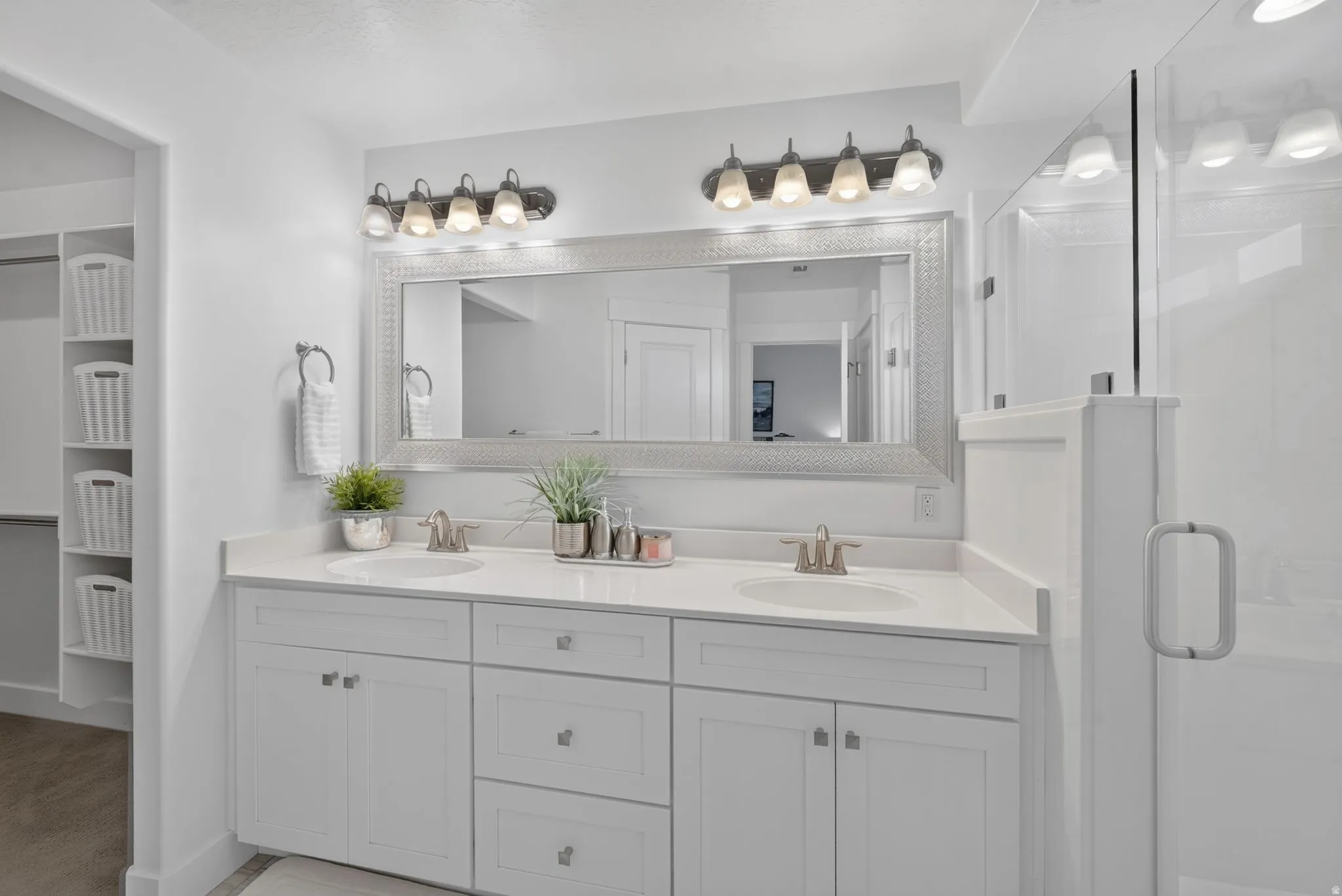 Dual vanity with integrated sinks, white cabinetry, a framed mirror, and an adjacent glass-enclosed shower