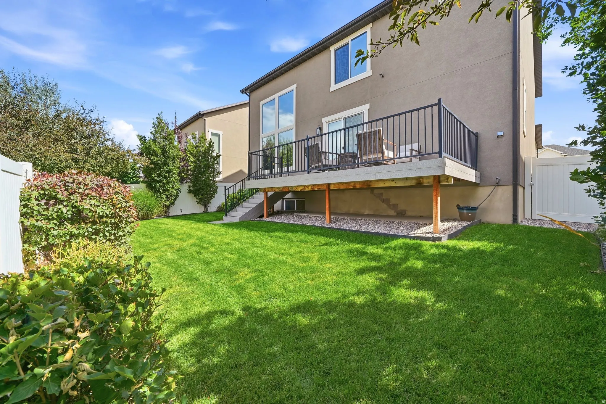 Expansive backyard with a manicured lawn, multi-level deck, white vinyl fencing, and mature landscaping