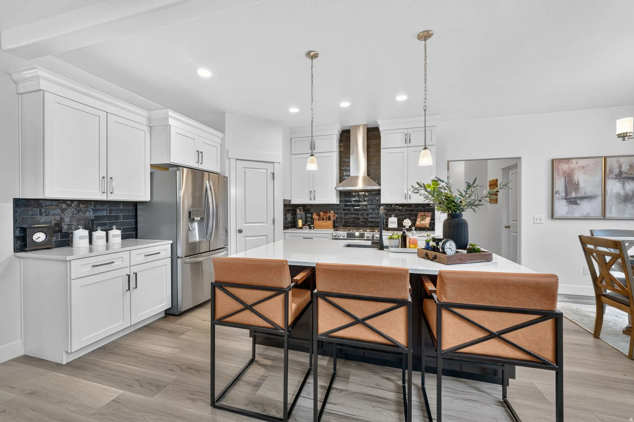 Bright kitchen featuring white shaker cabinetry, stainless steel appliances, a center island with pendant lighting, a dark tile backsplash, and wood-finish flooring