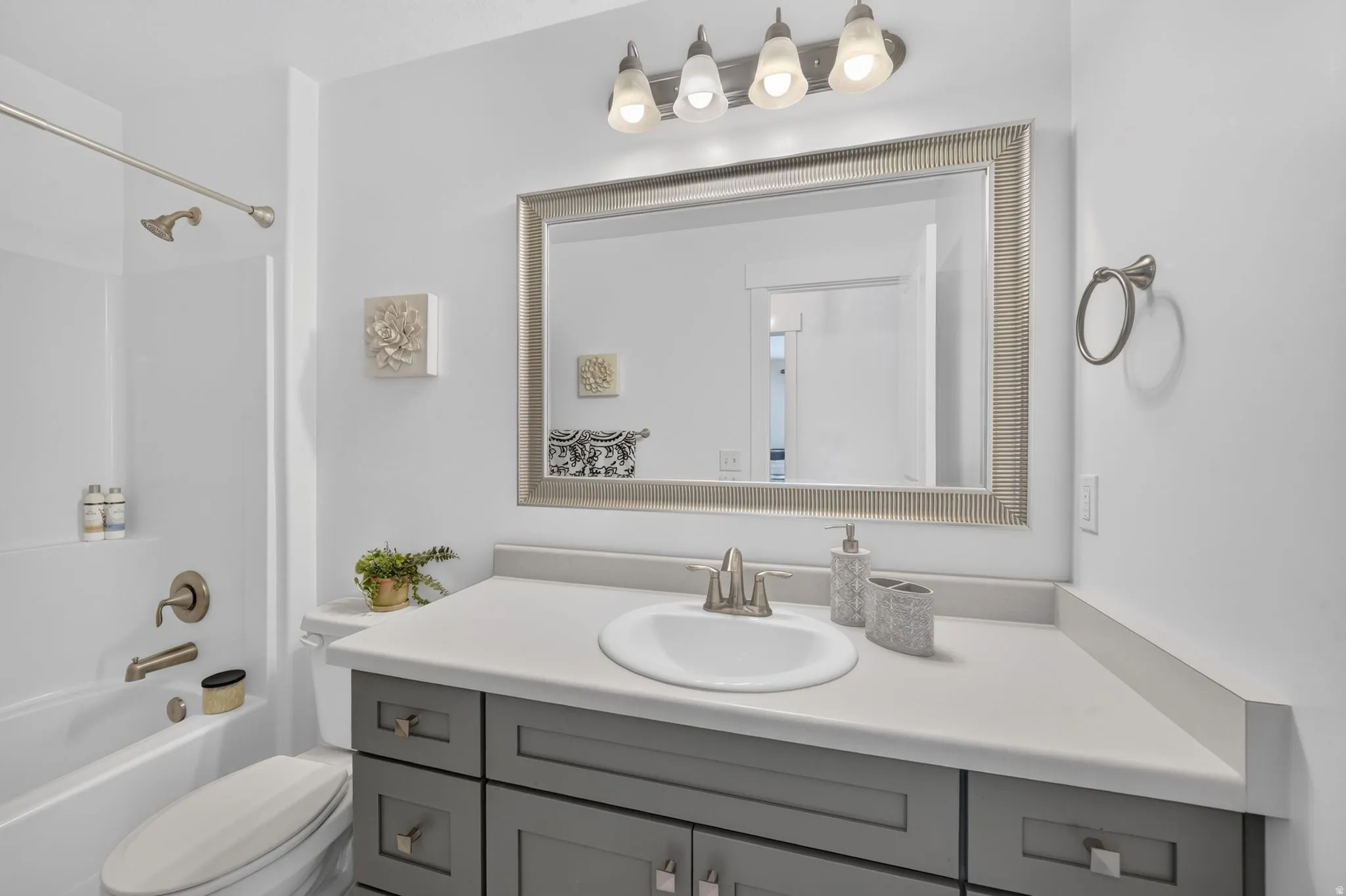 Bathroom featuring a white bathtub, brushed nickel fixtures, a gray vanity with an integrated sink, a large framed mirror, and a four-light fixture