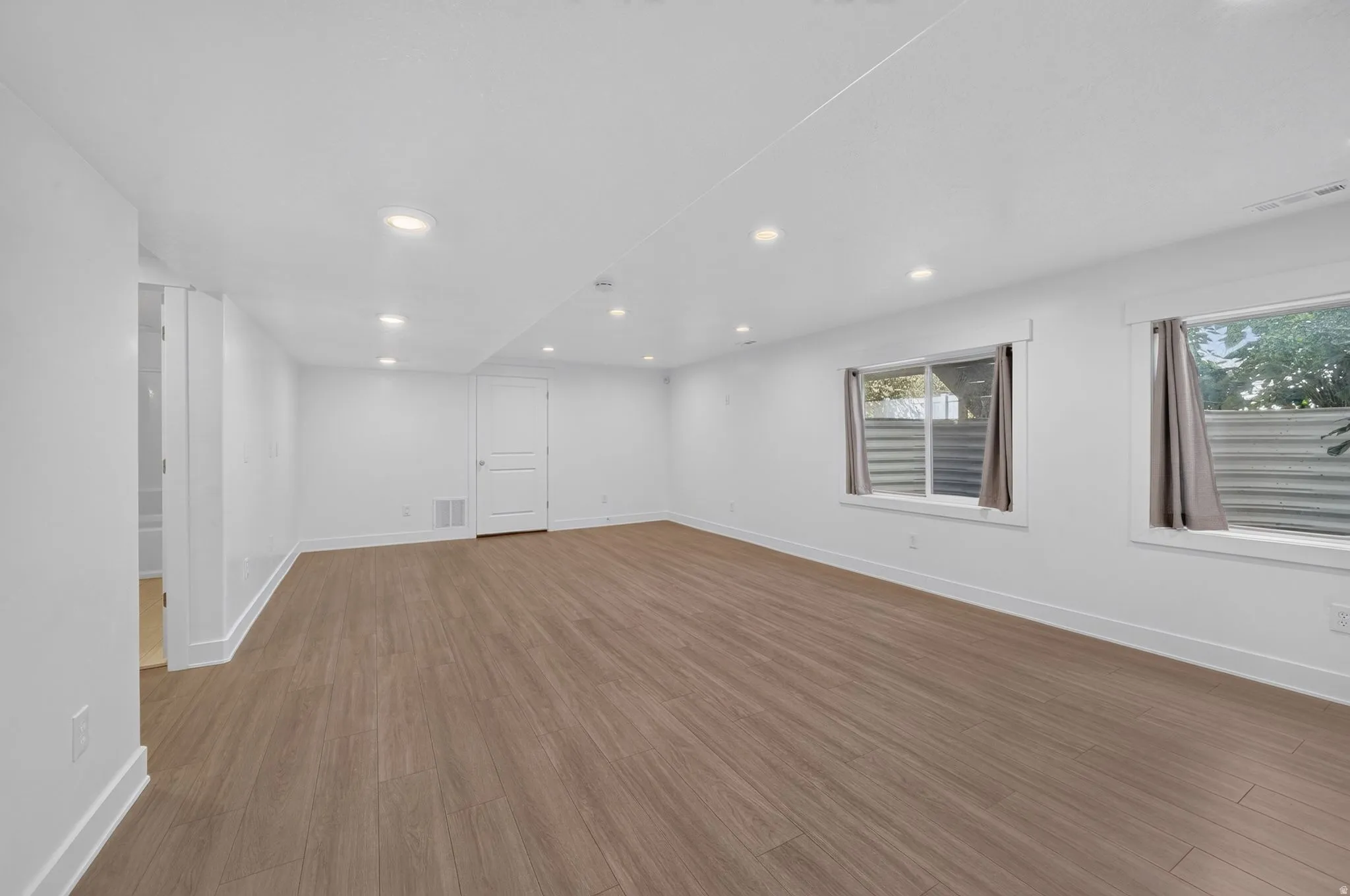 Basement Expansive room with wood-finish flooring, recessed lighting, white walls, and two windows