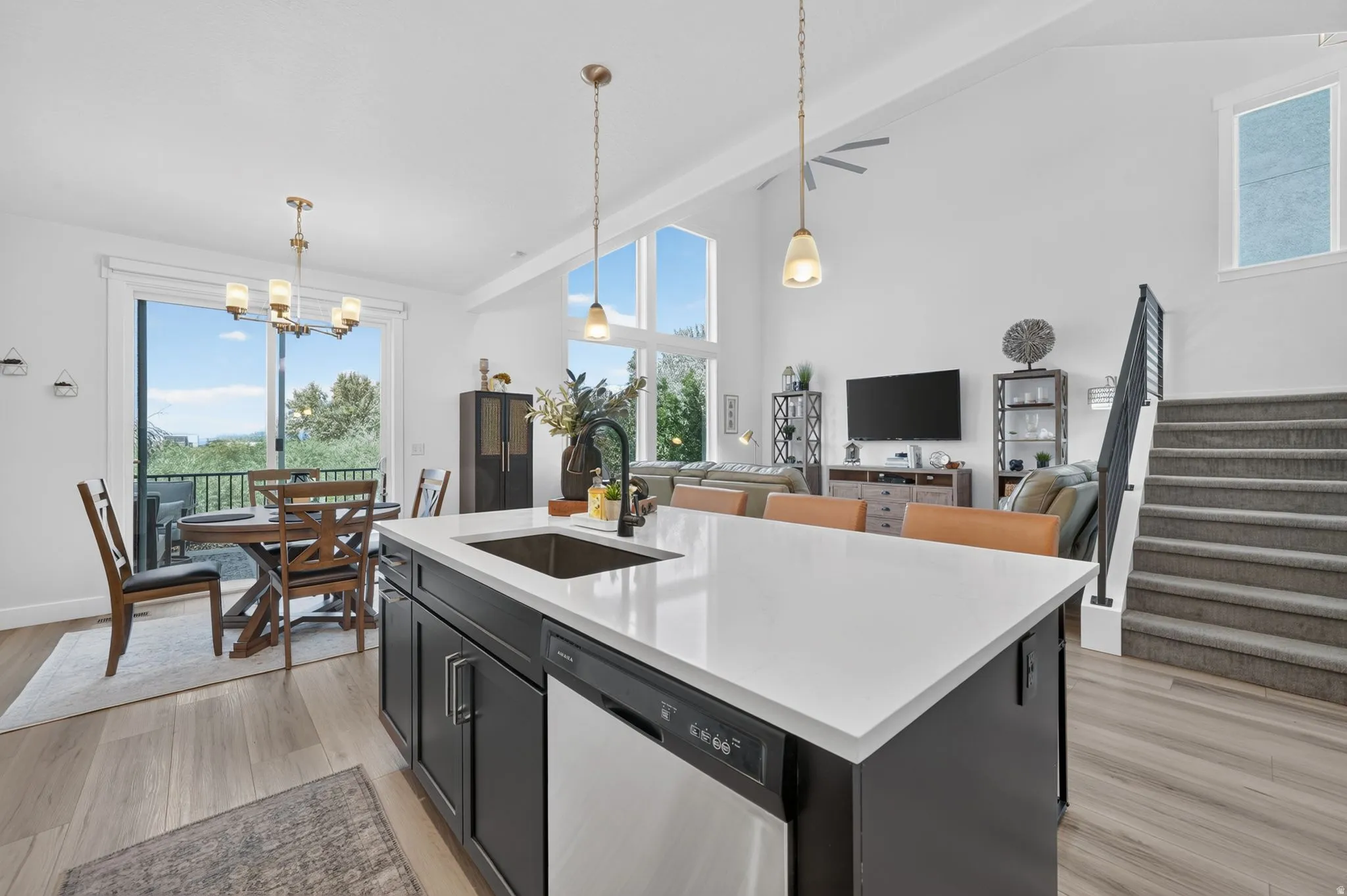 Open-concept living area with vaulted ceilings, wood-finish flooring, a kitchen island with seating, a stainless steel sink, and a deck