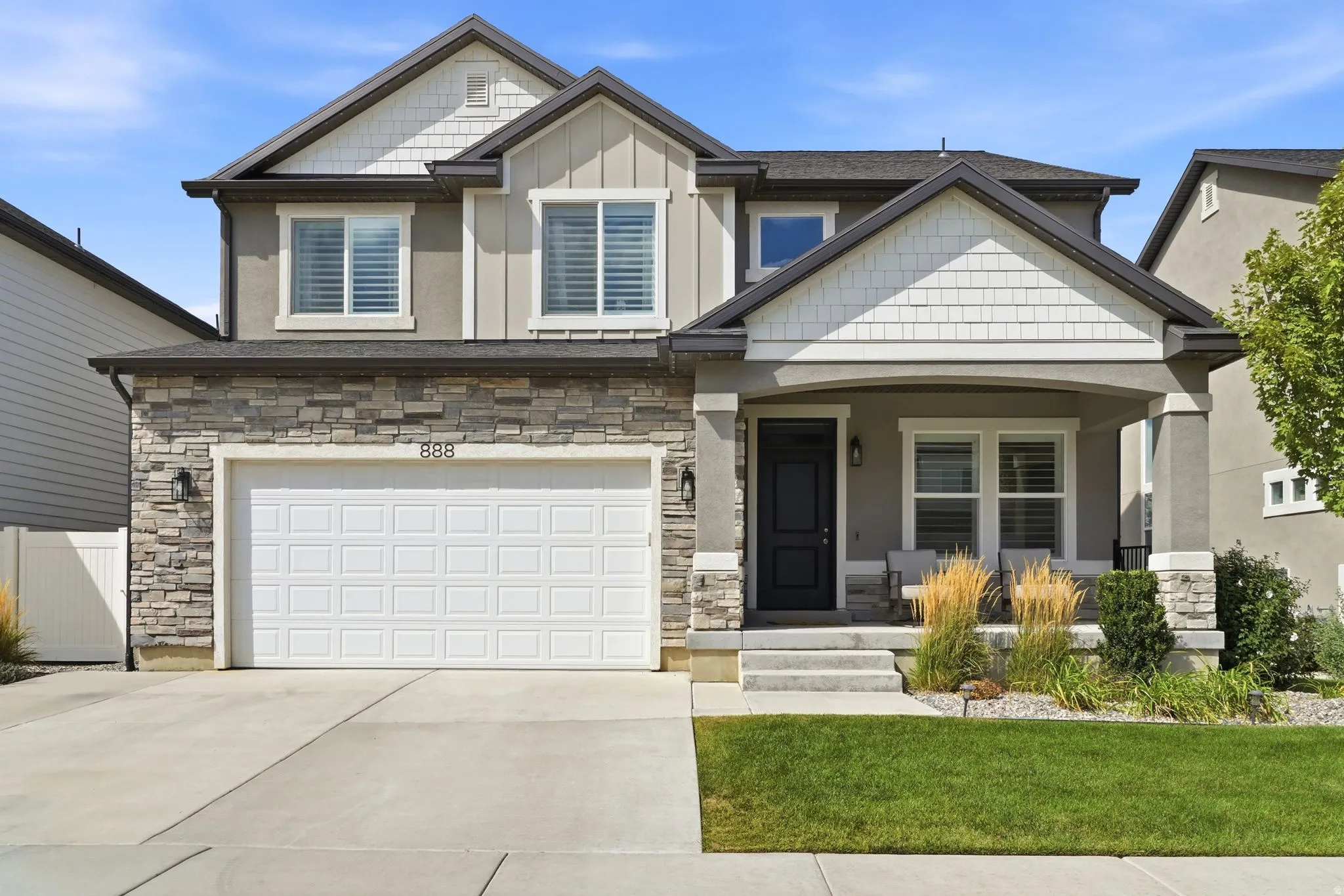 Two-story exterior with stone veneer accents, an attached two-car garage, covered porch, and mature front landscaping