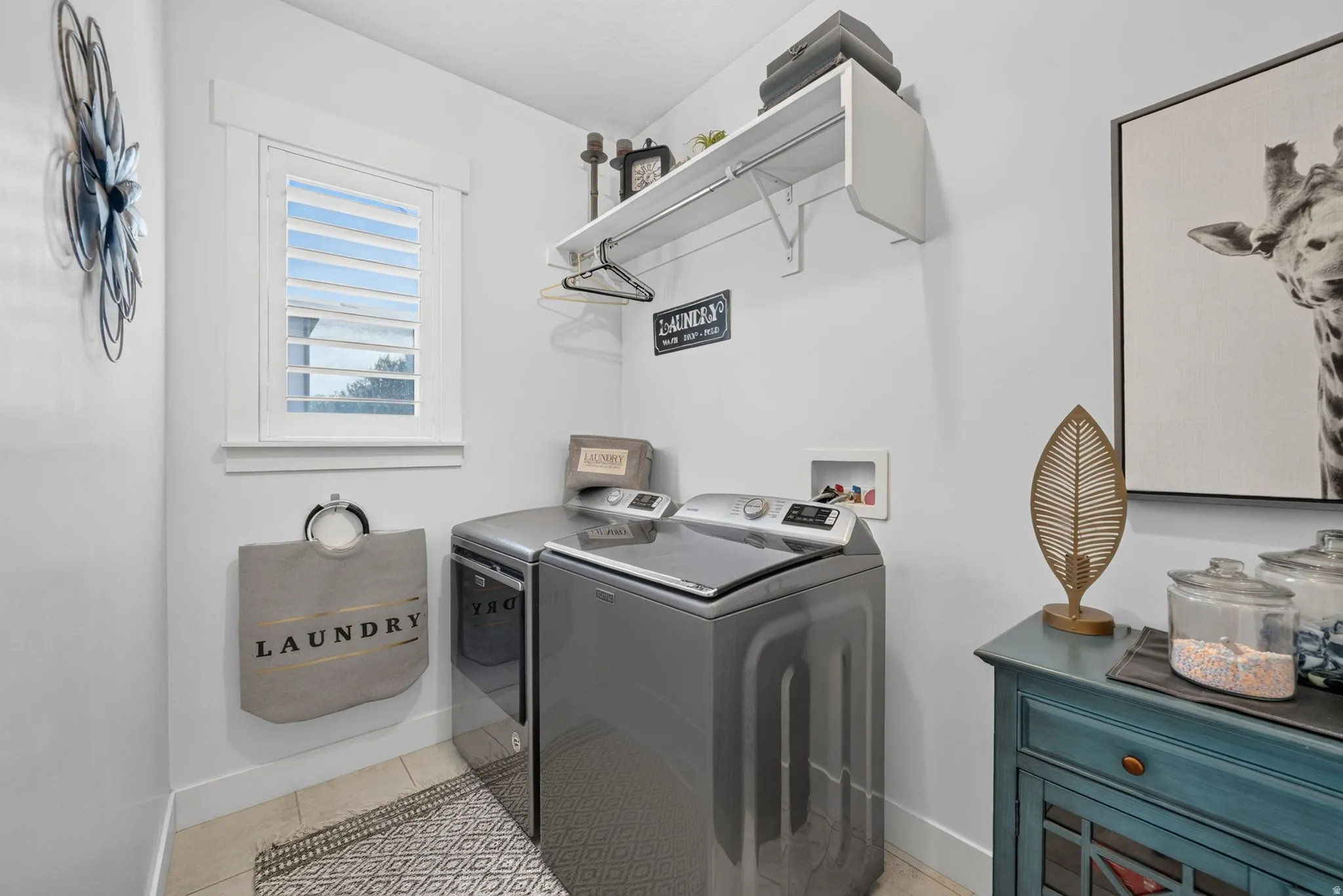 Laundry area featuring a window with white shutters, a built-in shelving unit, and tile flooring