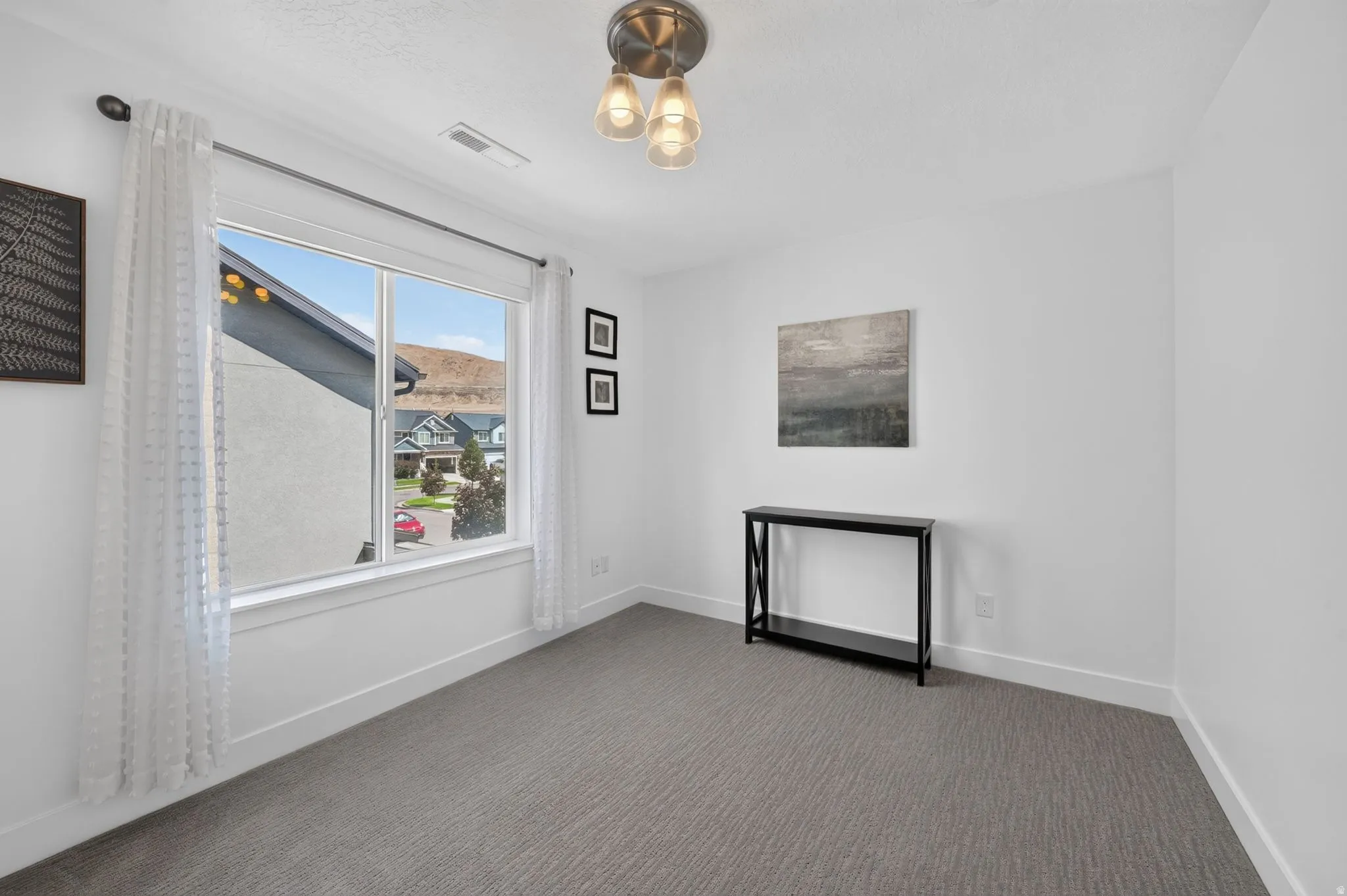 Recessed lighting, large window, neutral wall paint, gray patterned carpeting, and a contemporary ceiling fixture