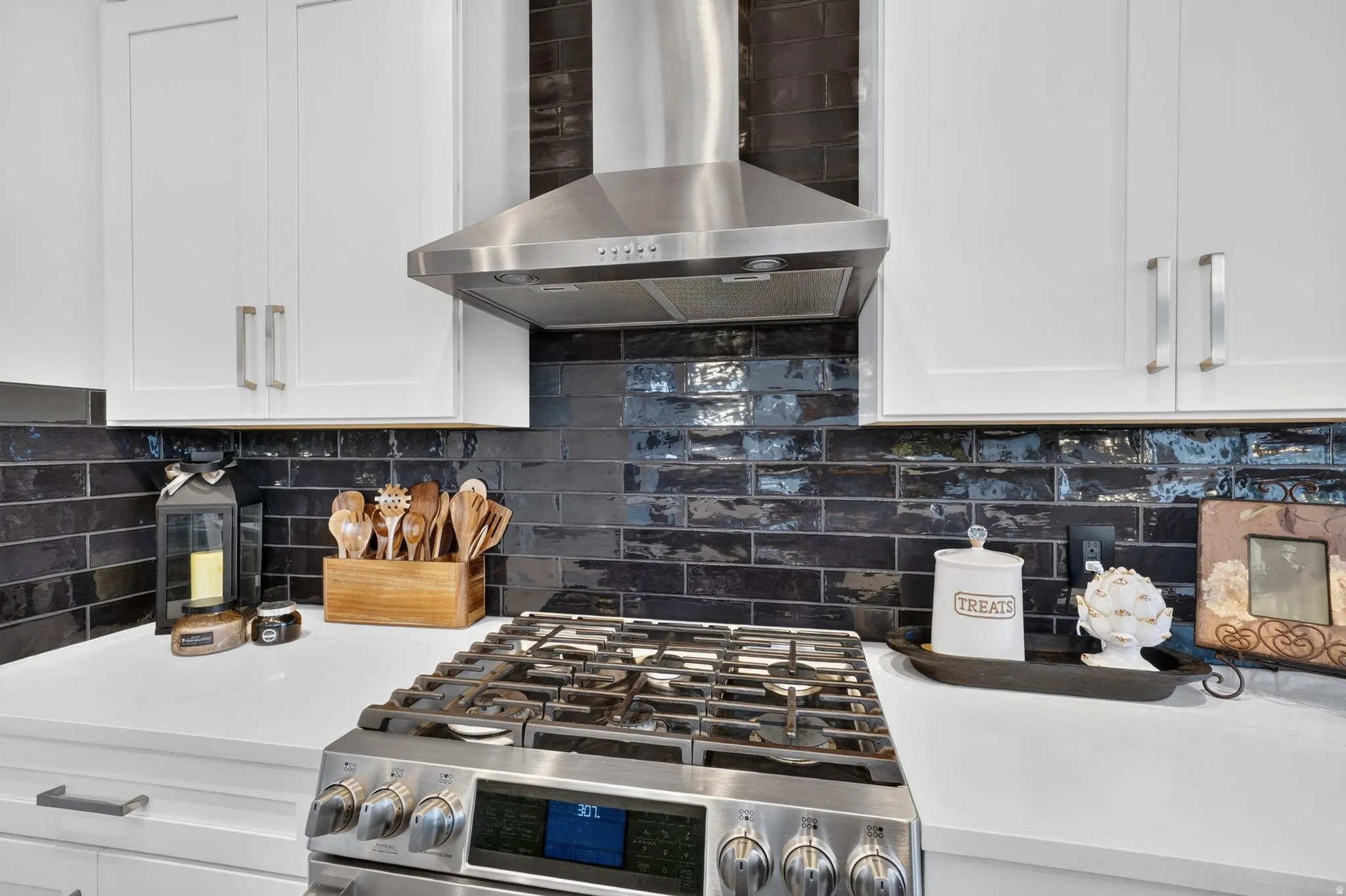 Stainless steel range hood, dark subway tile backsplash, white upper cabinetry, stainless steel range, and white countertop