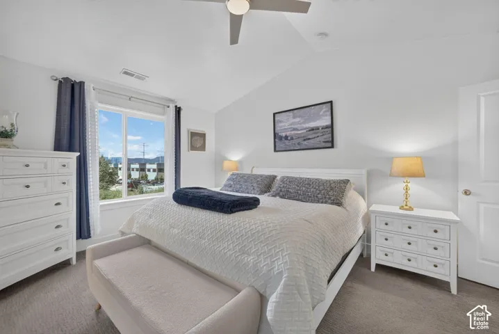 Bright, light-filled master bedroom featuring dual nightstands with brass table lamps, white cabinetry, ceiling fan, and expansive windows overlooking neighborhood streetscape