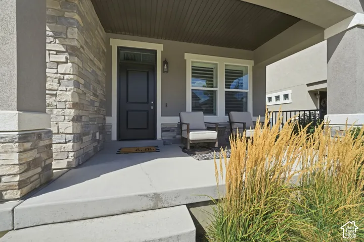 Covered porch featuring a paneled entry door, stone veneer accents, and stucco siding