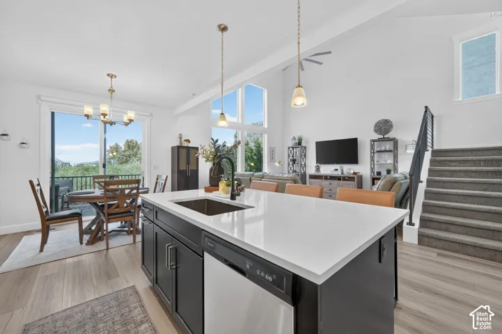 Open-concept living area with vaulted ceilings, wood-finish flooring, a kitchen island with seating, a stainless steel sink, and a deck