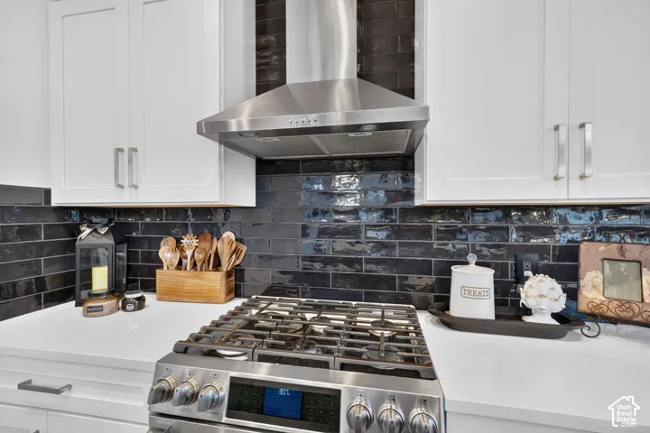 Stainless steel range hood, dark subway tile backsplash, white upper cabinetry, stainless steel range, and white countertop