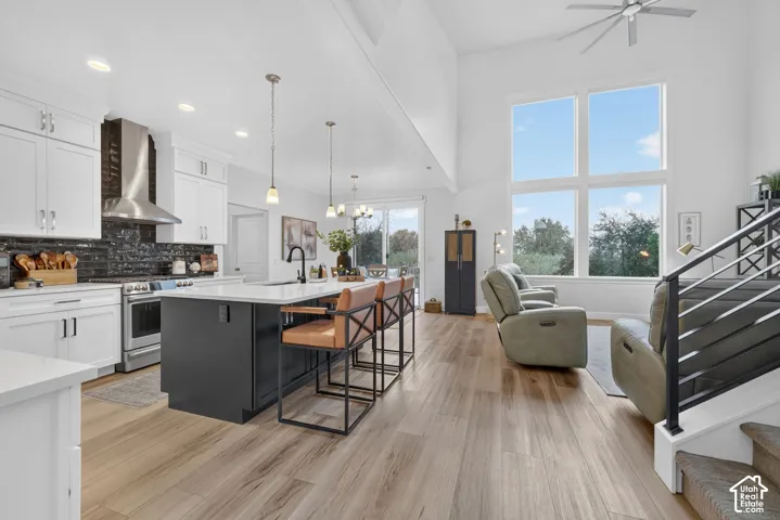 Open-concept interior featuring wood-finish flooring, white cabinetry, a kitchen island with seating, a stainless steel range hood, and a two-story window array