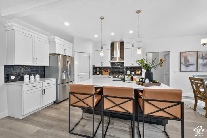 Bright kitchen featuring white shaker cabinetry, stainless steel appliances, a center island with pendant lighting, a dark tile backsplash, and wood-finish flooring