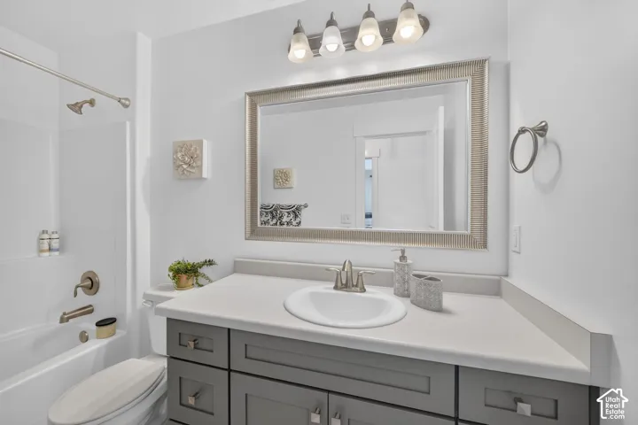 Bathroom featuring a white bathtub, brushed nickel fixtures, a gray vanity with an integrated sink, a large framed mirror, and a four-light fixture