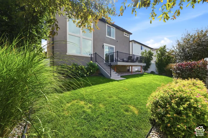 Expansive backyard featuring a manicured lawn, a raised deck with metal railings, a sliding glass door, and a stucco exterior