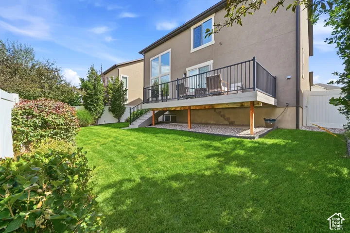 Expansive backyard with a manicured lawn, multi-level deck, white vinyl fencing, and mature landscaping