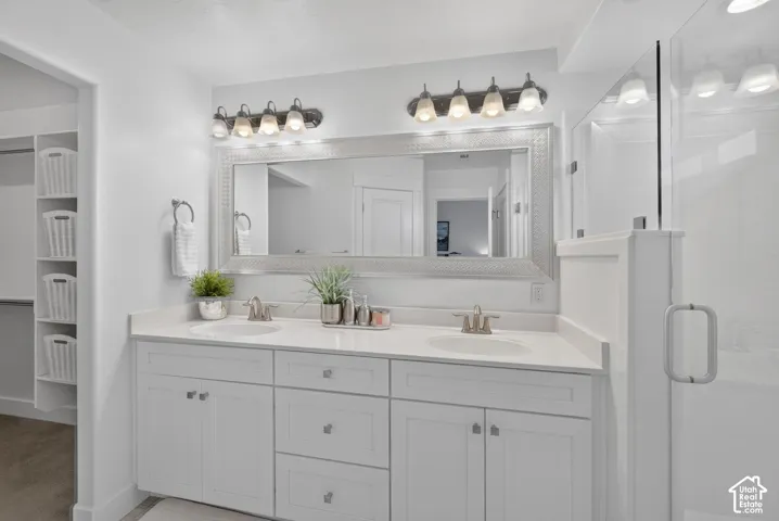 Dual vanity with integrated sinks, white cabinetry, a framed mirror, and an adjacent glass-enclosed shower