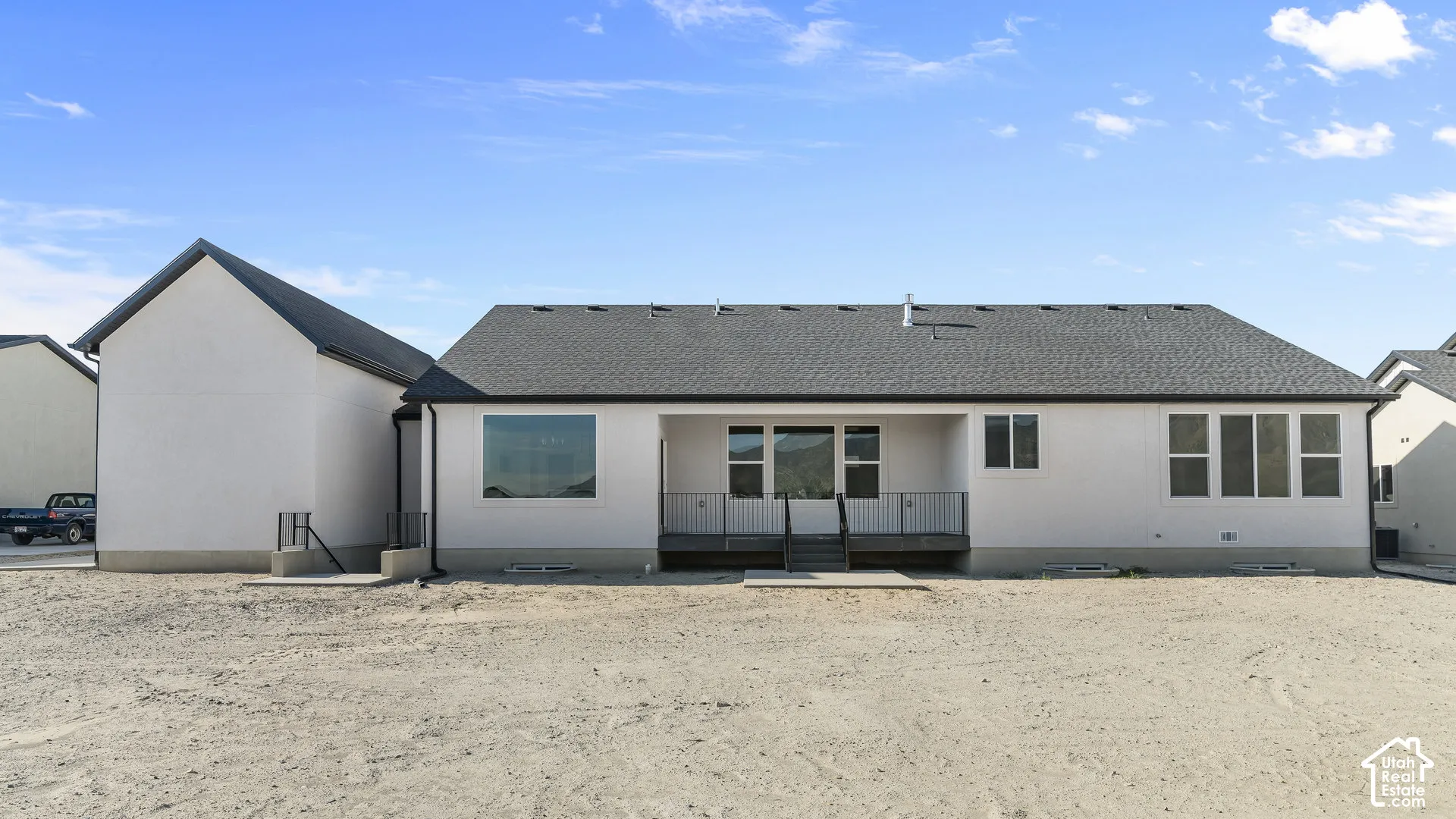 Rear exterior with white stucco finish, dark shingle roofing, and a prominent deck with black railings