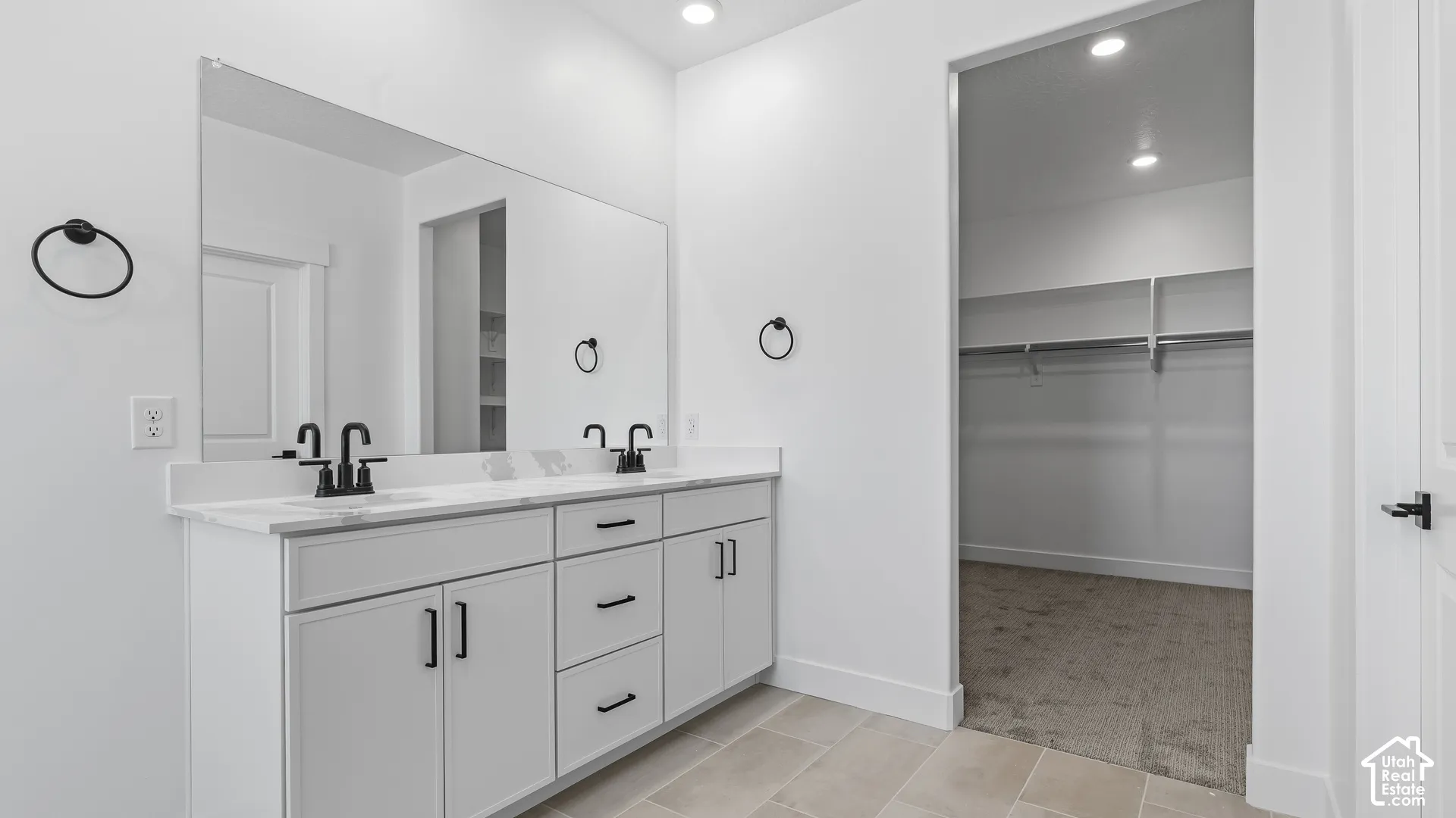 Dual vanity with white cabinetry, matte black fixtures, and a spacious walk-in closet with built-in shelving