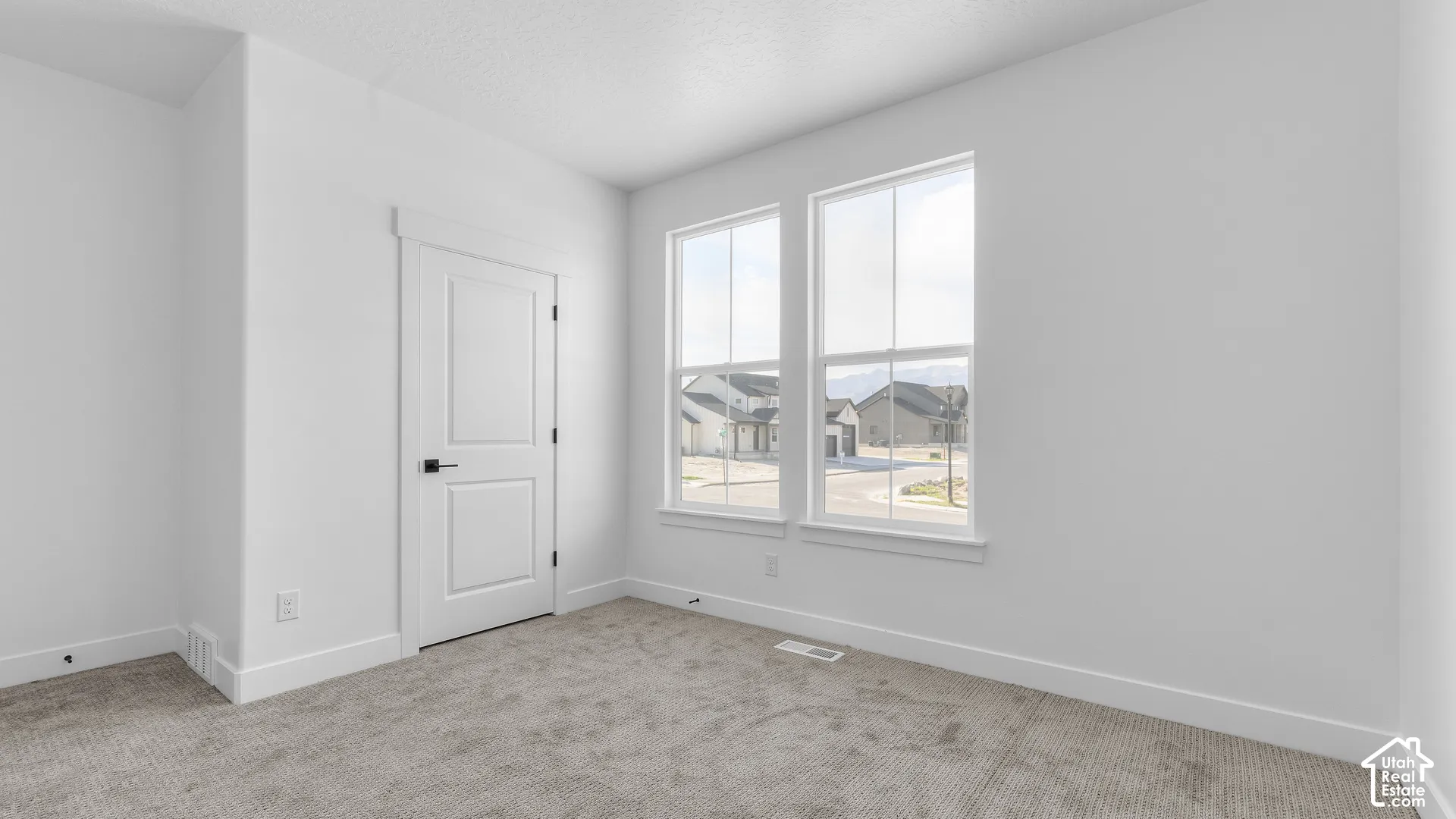 Neutral-toned carpeting paired with white walls, two windows, and a two-panel interior door with dark hardware