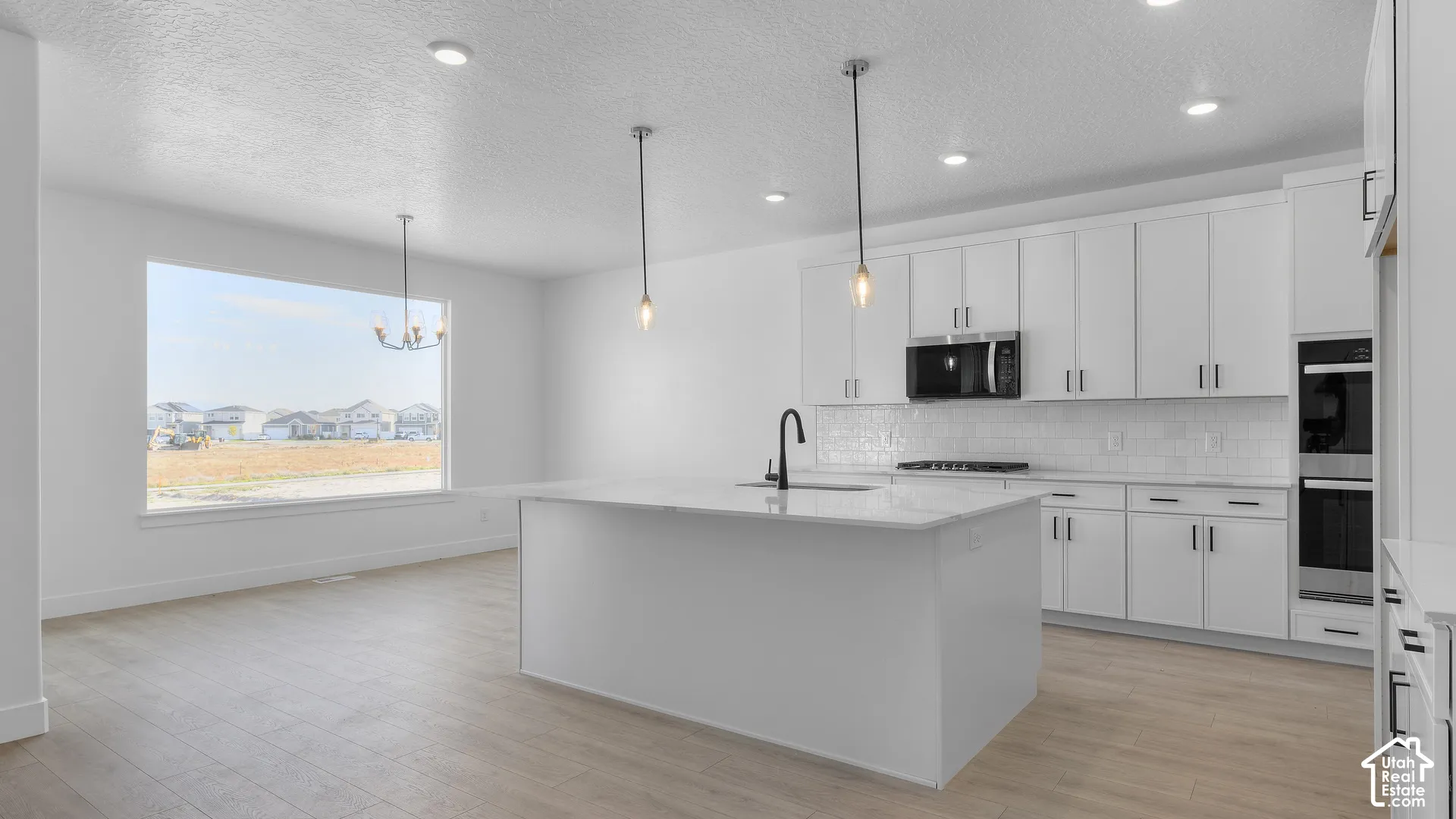 Kitchen featuring white cabinetry, a central island with a sink, stainless steel appliances, and wood-finish flooring