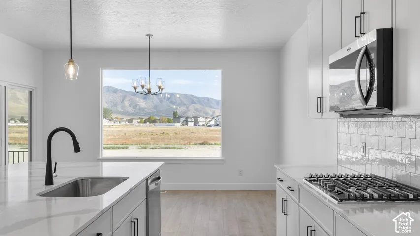 Open-concept kitchen featuring an integrated stainless steel sink, large window, pendant lighting, and light-toned cabinetry with dark hardware