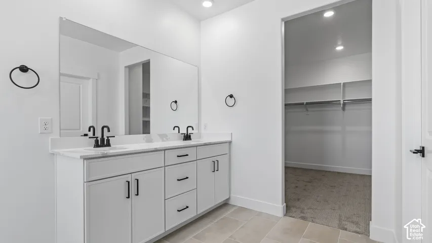 Dual vanity with white cabinetry, matte black fixtures, and a spacious walk-in closet with built-in shelving