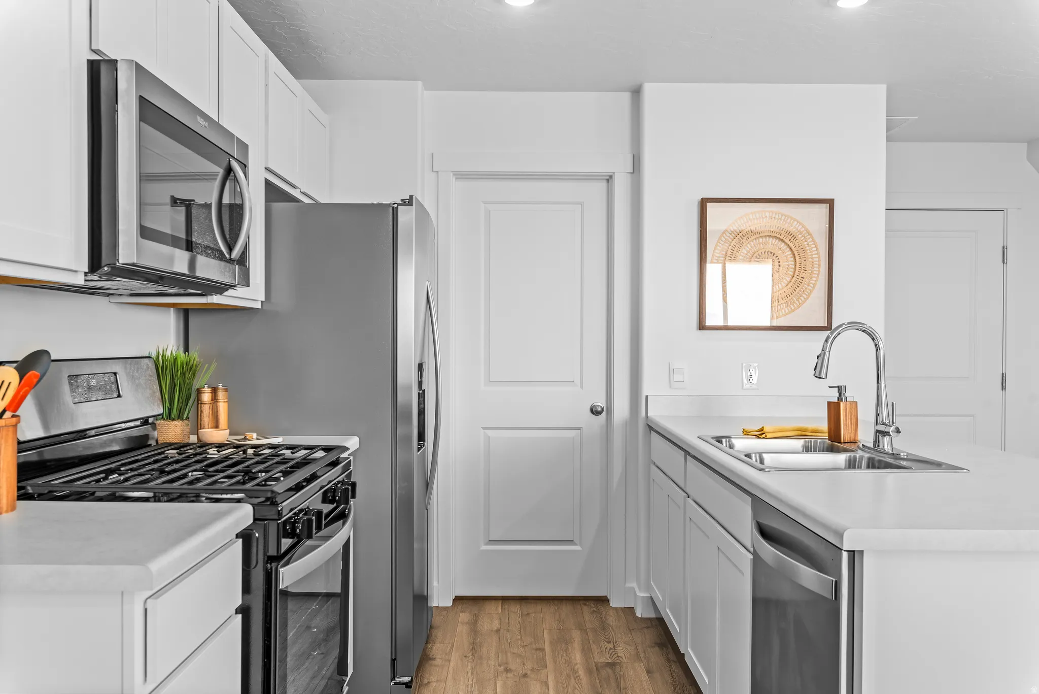 White cabinetry with stainless steel appliances, including an over-range microwave, refrigerator, gas range, and built-in dishwasher