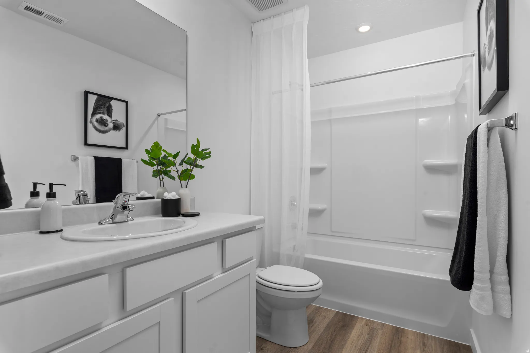 Bathroom featuring a vanity with an integrated sink, polished chrome faucet, wood-finish flooring, a toilet, and a shower-tub combination with a white surround
