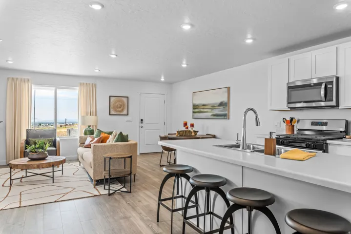 Open-concept living space featuring wood-finish flooring, recessed lighting, and a kitchen with white cabinetry, stainless steel appliances, and a breakfast bar
