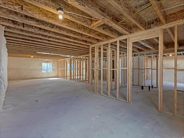 Unfinished basement with concrete flooring, exposed wood ceiling joists, framed interior walls, visible electrical wiring, and a window opening