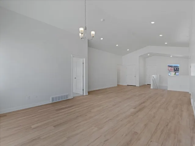 Vaulted ceilings, recessed lighting, wood-finish flooring, white doors, and a decorative chandelier