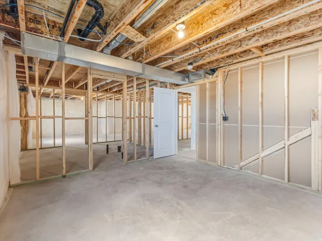 Spacious unfinished basement with exposed wood-beam ceiling, concrete flooring, and framed partition walls ready for customization