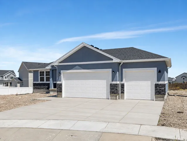 Contemporary exterior with light blue stucco and dark stone accents, featuring a two-car garage, concrete driveway, and a gabled roof