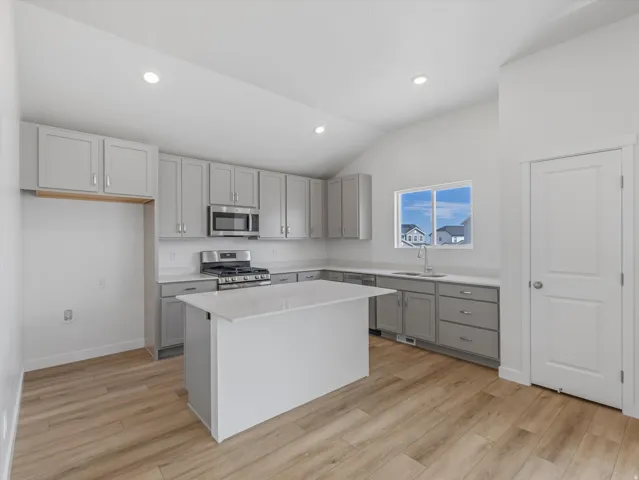 Vaulted ceiling, recessed lighting, wood-finish flooring, central island with solid surface countertop, and stainless steel appliances