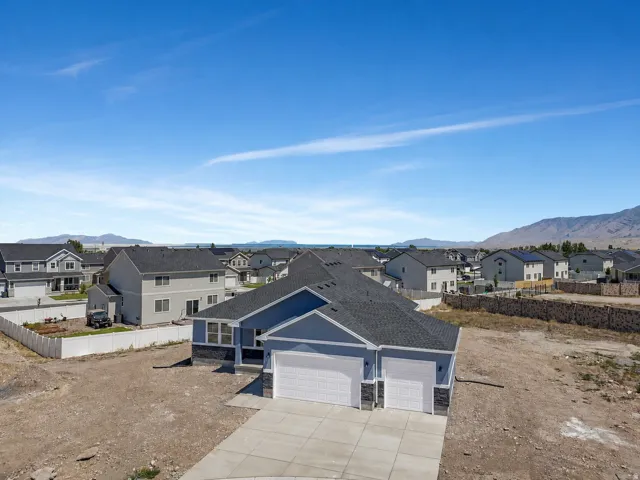 Modern construction featuring a blue exterior with stone accents, a dark shingle roof, and a multi-car garage with white doors