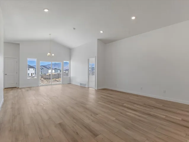 Vaulted ceiling with recessed lighting, wood-finish flooring, sliding glass door, multiple windows, and a chandelier