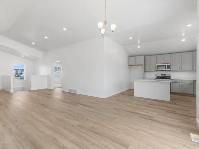 Vaulted ceilings with recessed lighting, wood-finish flooring, and a kitchen featuring gray cabinetry, stainless steel appliances, and a central island