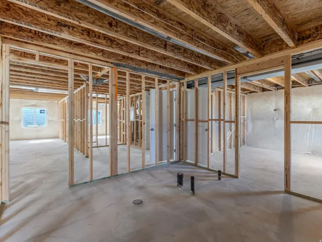 Unfinished basement with wood framing, exposed joists, concrete flooring, and egress windows