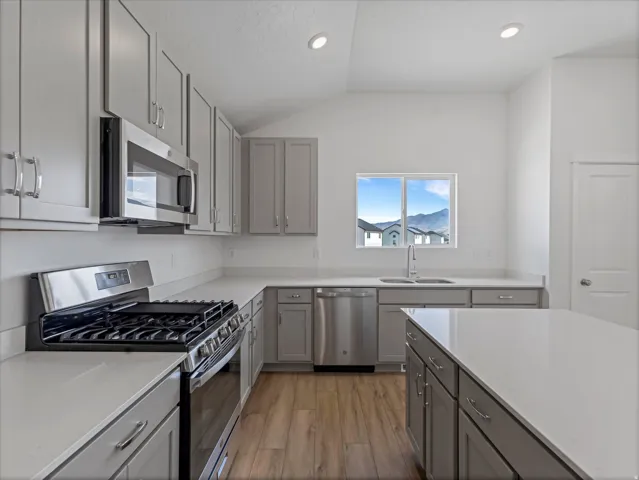 Modern kitchen featuring a gas range, stainless steel appliances, light gray cabinetry, light countertops, and wood-finish flooring