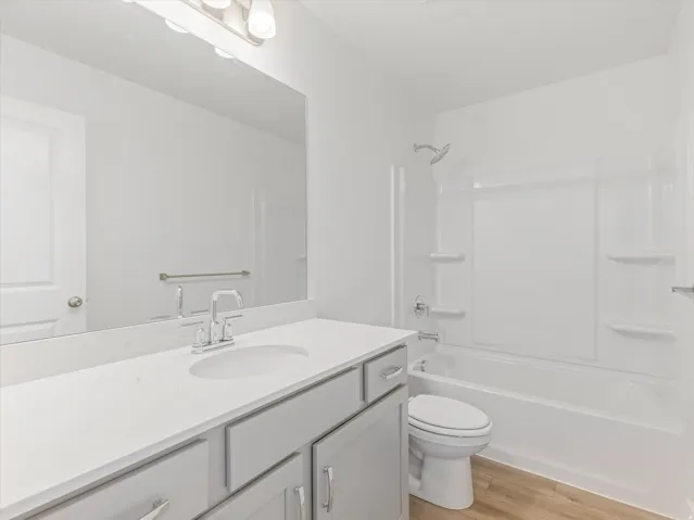 Light gray vanity with brushed nickel hardware, white countertop with integrated sink, chrome faucet, and white tub/shower combination