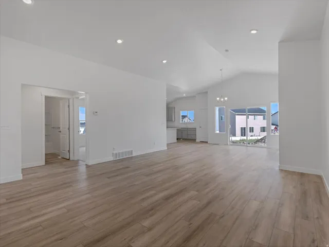 Expansive open-concept living area featuring high vaulted ceilings, wood-finish flooring, recessed lighting, and a sliding glass door