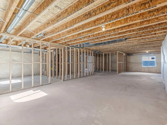 Unfinished lower level with wood framing, exposed ceiling joists, concrete flooring, and an egress window