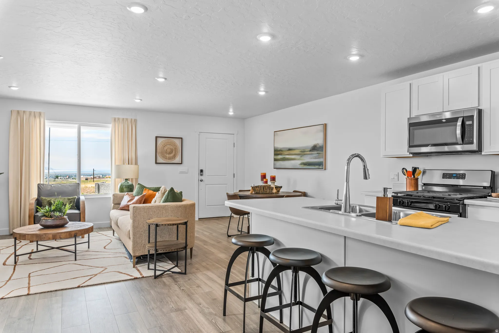 Open-concept living space featuring wood-finish flooring, recessed lighting, and a kitchen with white cabinetry, stainless steel appliances, and a breakfast bar