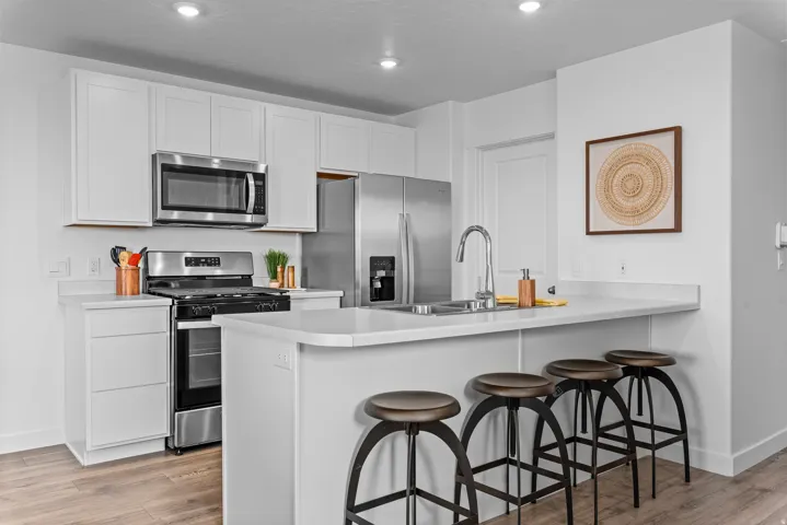 White cabinetry, stainless steel appliances, wood-finish flooring, recessed lighting, and a kitchen island with seating