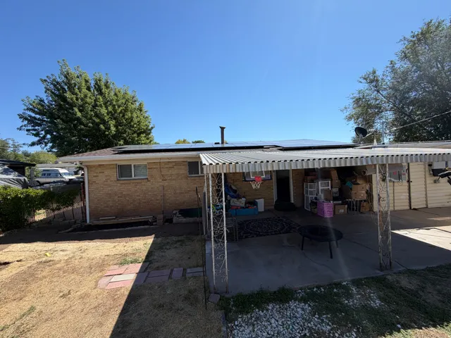 Rear exterior featuring a brick facade, rooftop solar panels, covered patio, and concrete patio flooring
