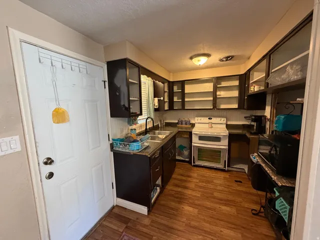 U-shaped kitchen with dark wood-finish cabinetry, wood-finish flooring, white beadboard backsplash, white range, and a dual-basin sink